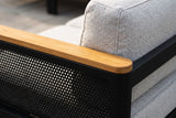Close-up of an Ognina arm: the solid teak armrest over the black perforated aluminum mesh, beside a light grey textured back cushion