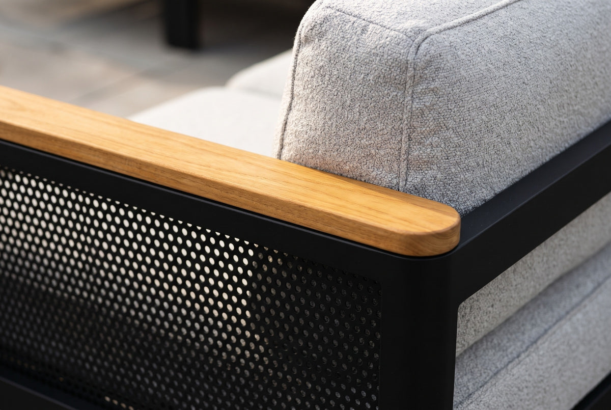 Close-up of an Ognina arm: the solid teak armrest over the black perforated aluminum mesh, beside a light grey textured back cushion