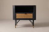 The Olbia nightstand in black acacia, front view on a light studio backdrop: an open niche above one cane drawer, on four slim black legs with brass caps