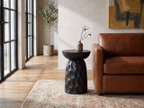 Olevano Carved Black Mango Pedestal Side Table beside a leather sofa in an industrial loft