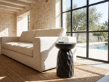 Olevano Carved Black Mango Pedestal Side Table beside a linen sofa in a poolside villa