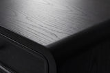 Close-up of the Oliena nightstand top: satin black painted wood with fine open grain, the raised drawer border and the rounded top corner