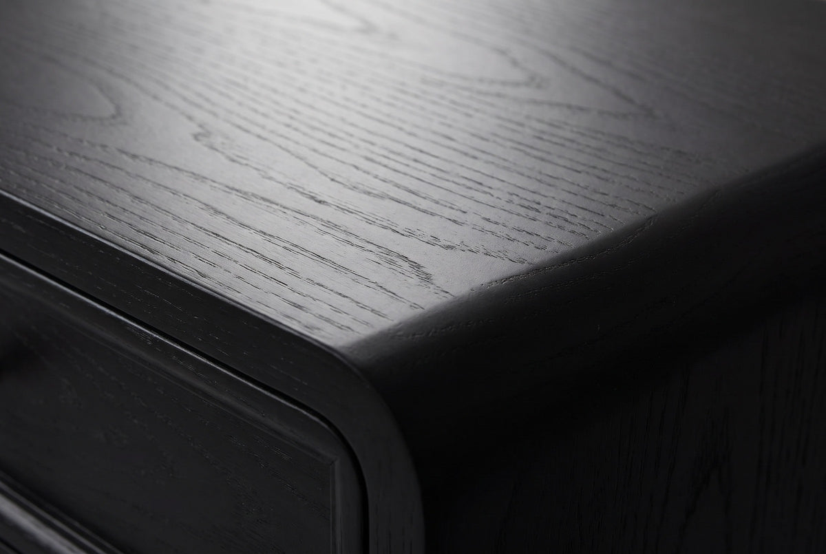 Close-up of the Oliena nightstand top: satin black painted wood with fine open grain, the raised drawer border and the rounded top corner