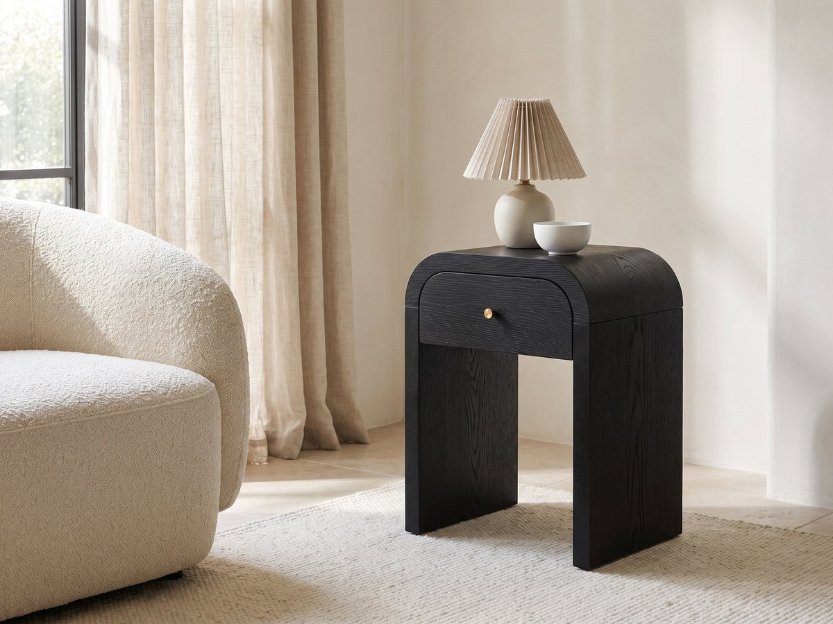 Oppido Black Ash Veneer Waterfall Side Table with a lamp and a ceramic bowl beside a cream boucle armchair in a bright plaster room