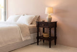 Orani dark winewood nightstand with a lit ceramic lamp and a woven basket against a dusty-pink plaster wall in a Palm Springs bedroom with a terrazzo floor