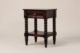 The Orani dark winewood nightstand with one drawer, a round brass knob, four turned bobbin legs and an open lower shelf, three-quarter view on a warm greige studio backdrop