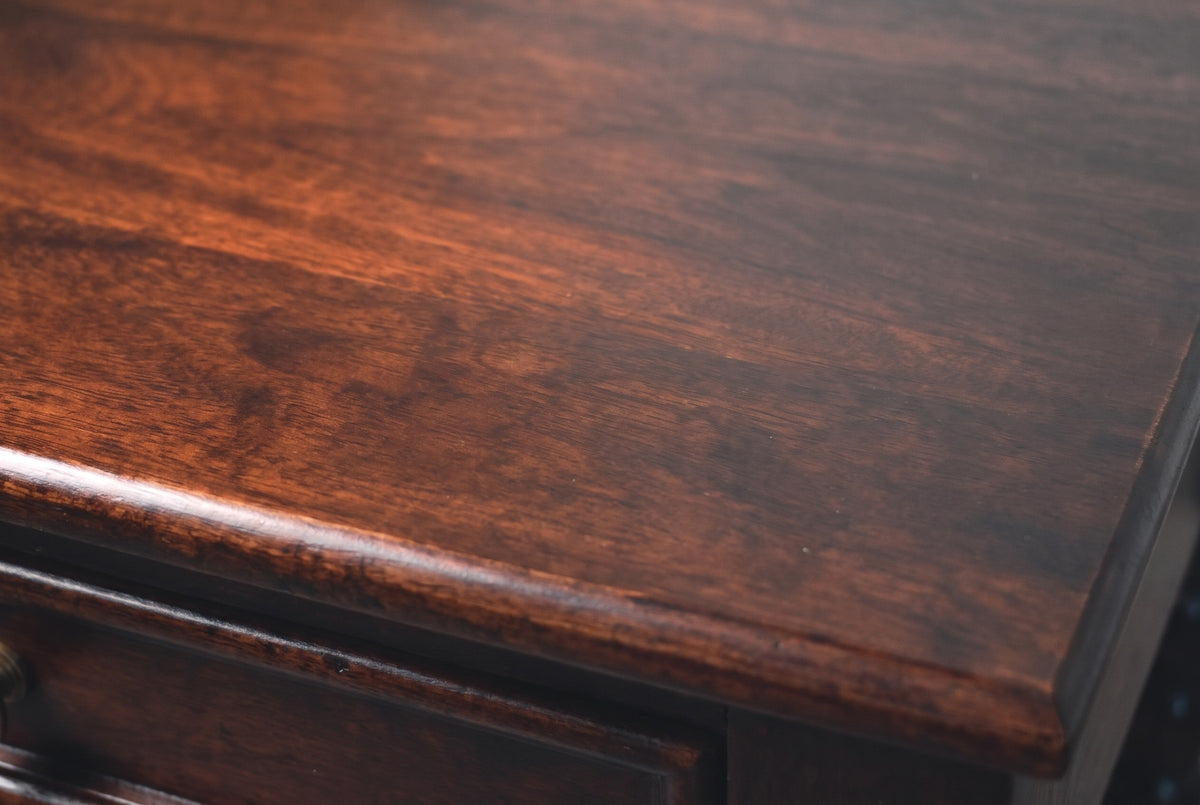 Close-up of the Orani nightstand top: dark winewood mango with soft flowing grain and a soft sheen, with the softly rounded edge of the top below