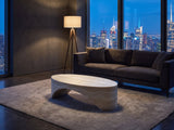 Orbetello Faux Travertine Oval Arch Coffee Table seen from the side, on a wool rug in front of a velvet sofa in a city penthouse at blue hour