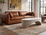 Orbetello Faux Travertine Oval Arch Coffee Table on a vintage rug in front of a leather sofa in an industrial loft