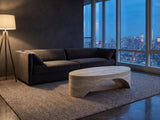 Orbetello Faux Travertine Oval Arch Coffee Table on a wool rug in front of a velvet sofa in a city penthouse at blue hour