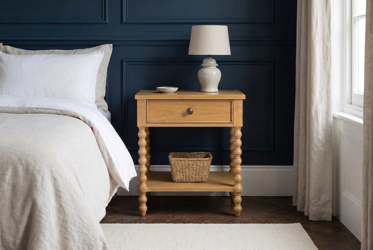 Orgosolo Camel Oak nightstand with a ceramic lamp and a seagrass basket against navy-blue panelled walls in a Boston brownstone bedroom with a dark herringbone floor