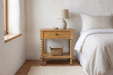 Orgosolo Camel Oak nightstand with a ceramic lamp and a seagrass basket against a white-washed adobe wall in a Santa Fe bedroom with a terracotta tile floor