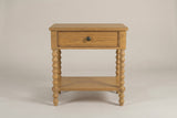 The Orgosolo Camel Oak nightstand, front view on a warm greige studio backdrop: a flat top, one drawer with one knob, four turned bobbin legs and an open shelf