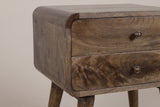 The front corner of the Oristano nightstand: the top rolling over a rounded corner of curved mango blocks, two flush drawers with their bronze-tone knobs and the top of a tapered leg