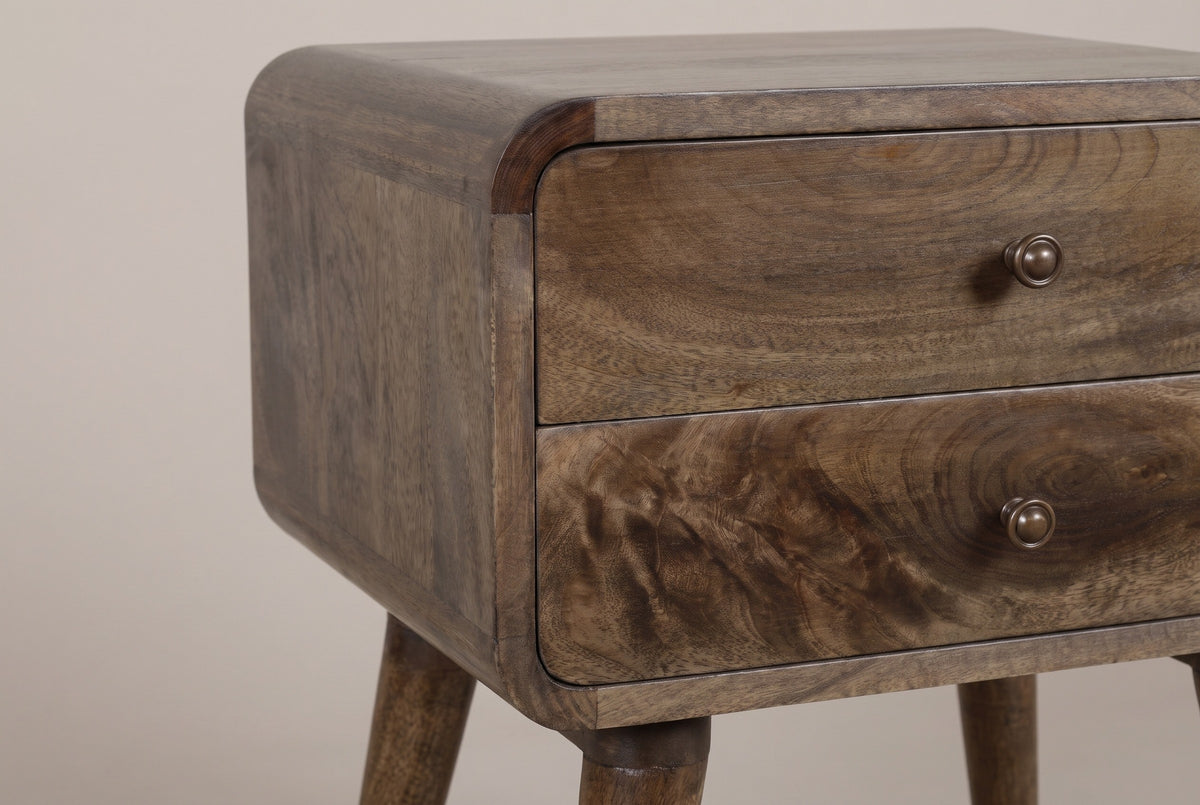 The front corner of the Oristano nightstand: the top rolling over a rounded corner of curved mango blocks, two flush drawers with their bronze-tone knobs and the top of a tapered leg
