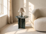 Orosei Verde Marble Round Side Table with a lamp and a ceramic bowl beside a cream boucle armchair in a bright plaster room