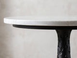 Close-up of the Orsara White Marble Pedestal Side Table: the white marble top edge over the hammered black base