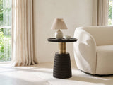 Orsomarso Carved Black Mango Pedestal Side Table with a lamp and a ceramic bowl beside a cream boucle armchair in a bright plaster room