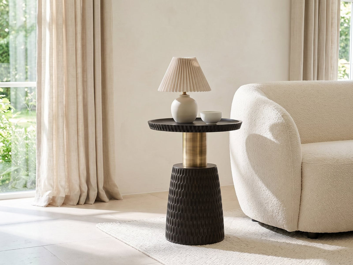 Orsomarso Carved Black Mango Pedestal Side Table with a lamp and a ceramic bowl beside a cream boucle armchair in a bright plaster room