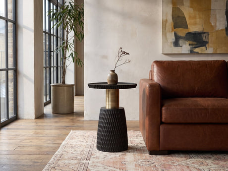 Orsomarso Carved Black Mango Pedestal Side Table beside a leather sofa in an industrial loft