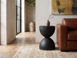 Orta Burnt Mango Hourglass Side Table beside a leather sofa in an industrial loft
