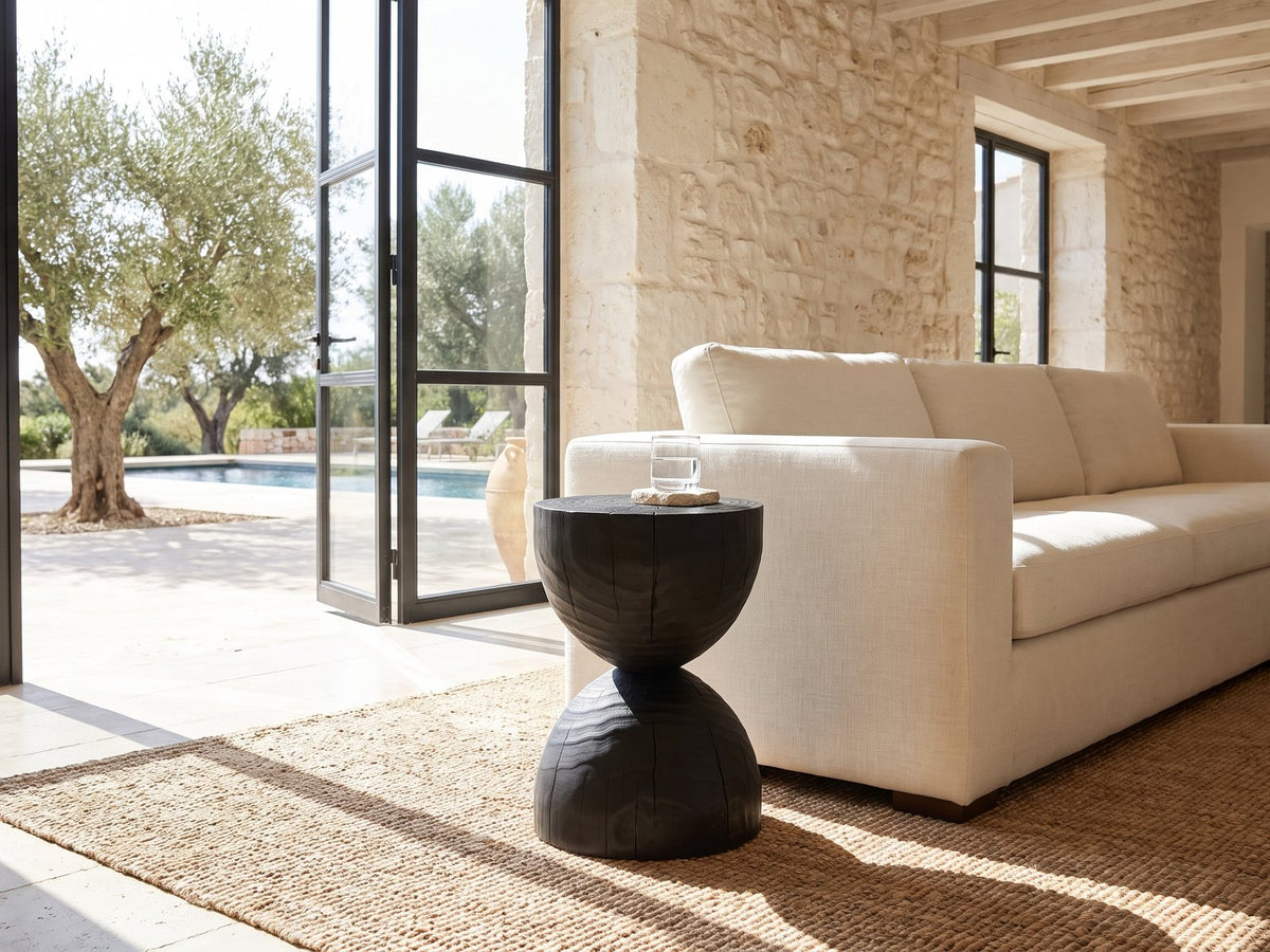 Orta Burnt Mango Hourglass Side Table beside a linen sofa in a poolside villa