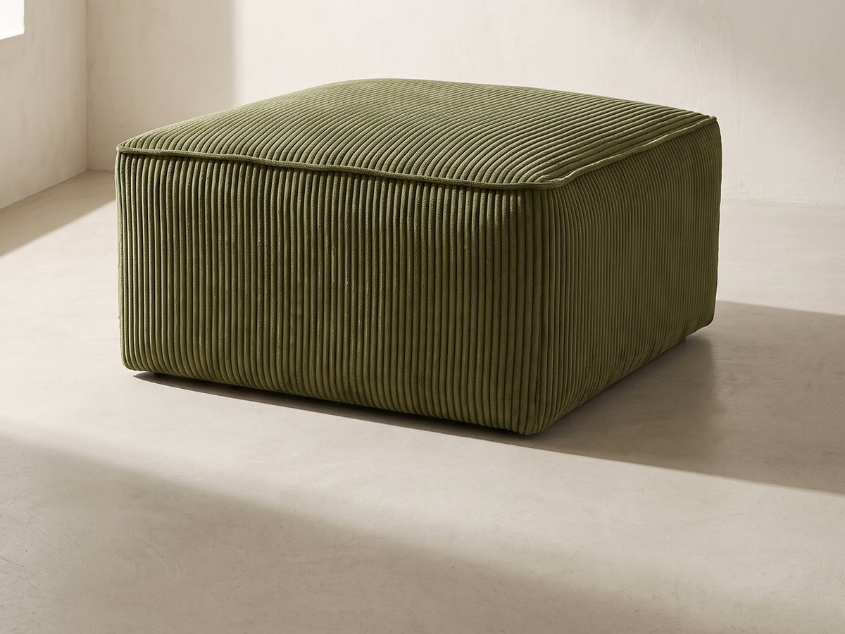 Orvieto Corduroy Cocktail Ottoman in olive green against a plaster wall in morning light
