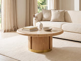 Ovada 35-Inch Round Sintered Stone and Wood Veneer Coffee Table styled with books, a vase and a stone bowl in front of a cream sofa in a bright plaster room