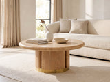 Ovada 35-Inch Round Sintered Stone and Wood Veneer Coffee Table seen from the side, styled with books, a vase and a stone bowl in front of a cream sofa in a bright plaster room