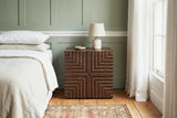 Ozieri walnut-brown ash nightstand with a lamp against a sage green panelled wall with a white picture rail in a Charleston bedroom with pine floorboards and a faded rug