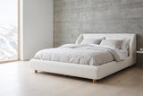 Pacentro white boucle low wingback bed against a board-formed concrete wall in an Aspen mountain bedroom, a tall window at the left looking onto snowy slopes