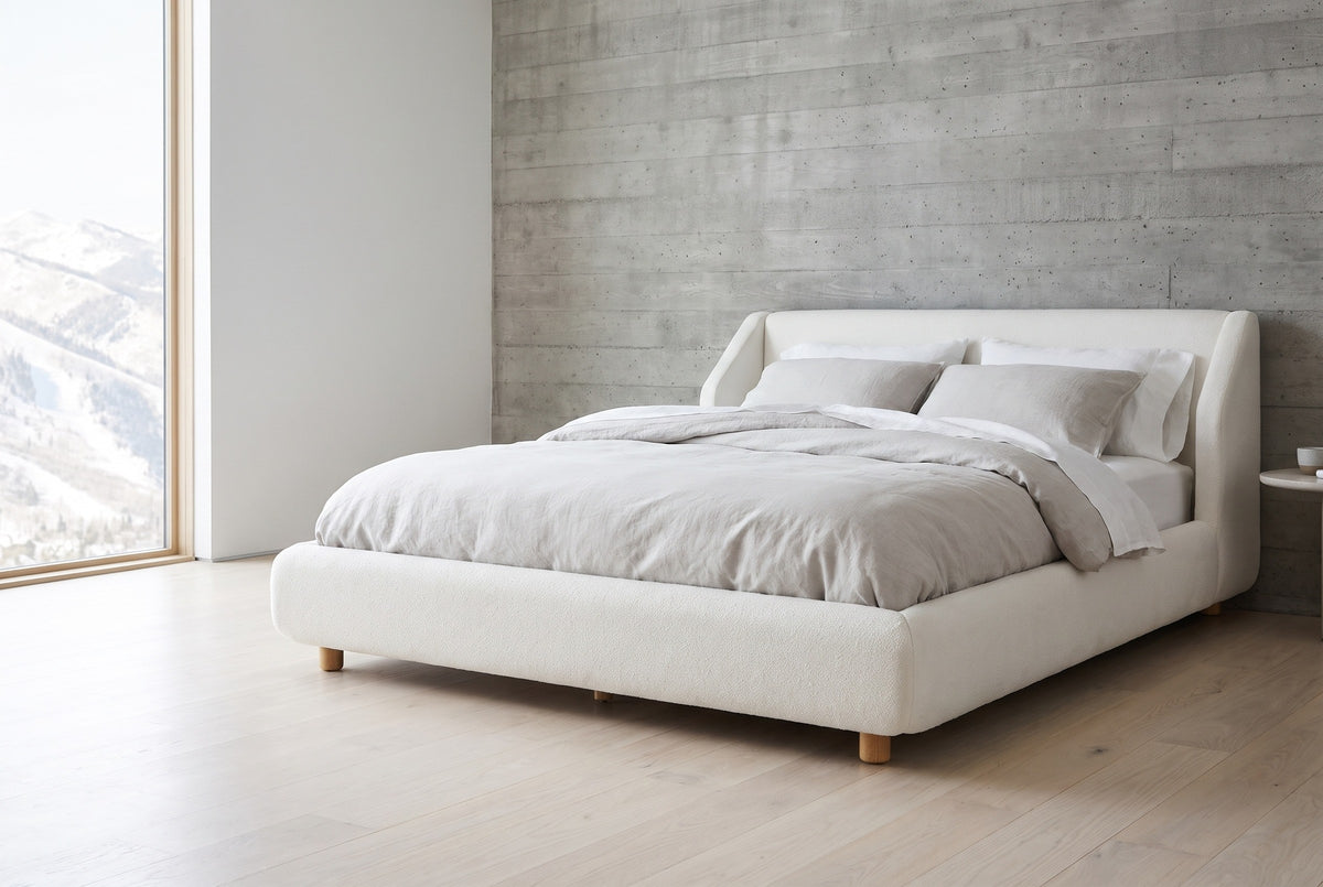 Pacentro white boucle low wingback bed against a board-formed concrete wall in an Aspen mountain bedroom, a tall window at the left looking onto snowy slopes