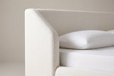 One side of the Pacentro headboard: the white boucle wing with a rounded top corner and a sloping front edge beside the plain flat panel, above a white pillow