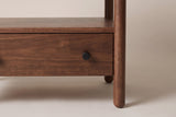 The lower drawer of the Palau nightstand: a small matte black knob on solid neem, with the open shelf above and a round post at the side