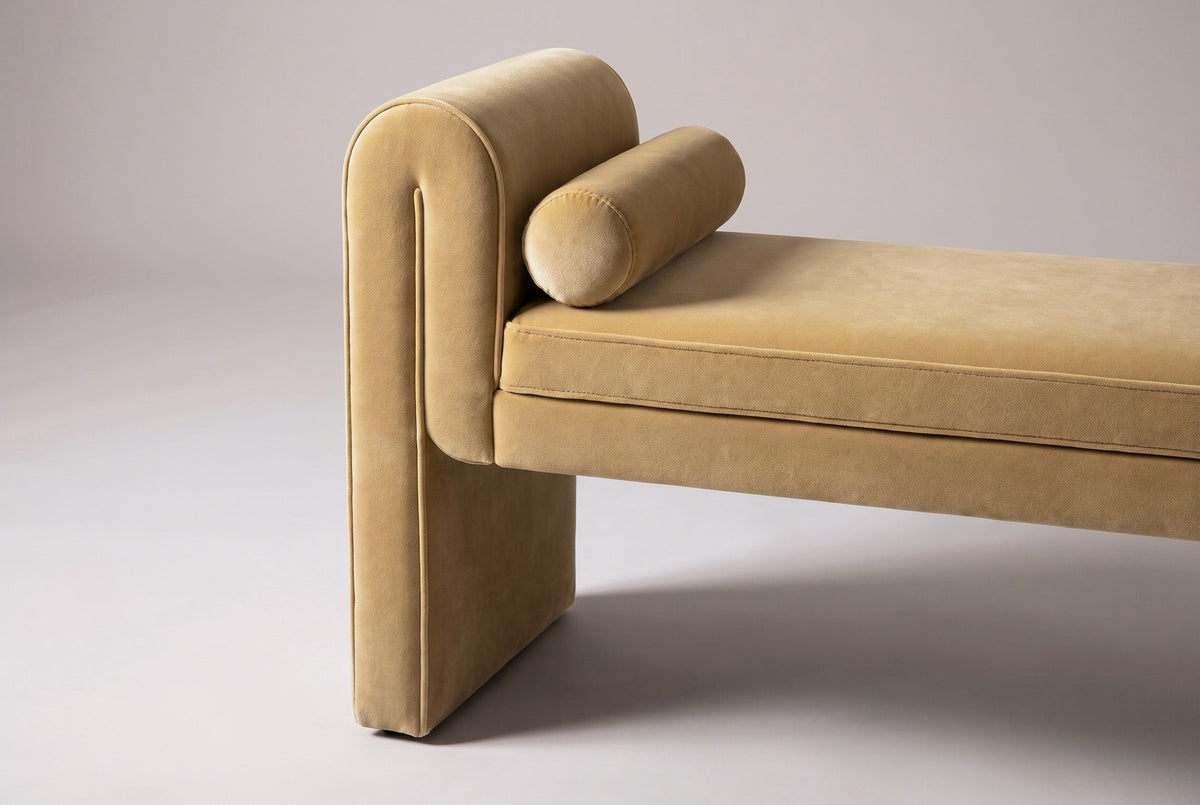 One end of the Panicale bench: the thick velvet panel with its arched top and thin welt, a round bolster lying against it and the piped edge of the seat beside it
