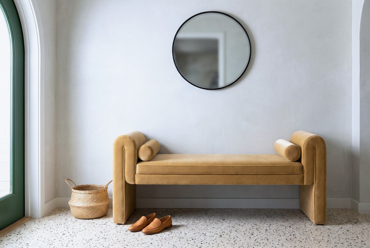 Panicale camel velvet bench against a pale limestone plaster wall in an Austin entry hall with a round black mirror, a terrazzo floor, a seagrass basket and a pair of loafers