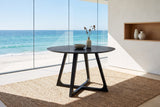 Paola 47.5-Inch Round Black Ash Dining Table in an oceanfront glass house