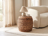 Parabita Woven Natural Fiber Barrel Side Table with a lamp and a ceramic bowl beside a cream boucle sofa in a bright plaster room