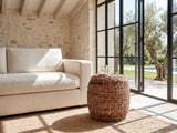 Parabita Woven Natural Fiber Barrel Side Table beside a linen sofa in a poolside villa
