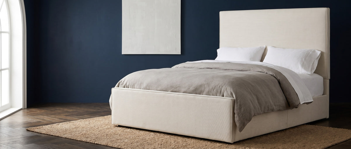 Penne ivory canvas bed with a tall plain headboard against an ink-navy wall in a Brooklyn brownstone loft, an arched window at the left