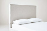 One side of the Penne headboard: a tall flat ivory canvas panel with a slim welt along its edge, above a white mattress with two white pillows