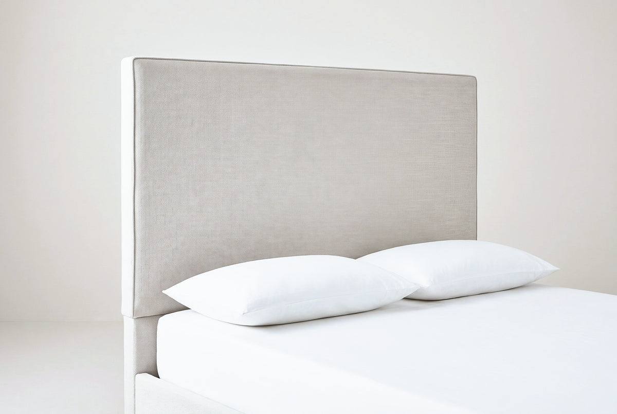 One side of the Penne headboard: a tall flat ivory canvas panel with a slim welt along its edge, above a white mattress with two white pillows
