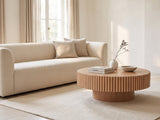 Pesaro Ash Veneer Fluted Pedestal Coffee Table styled with books, a vase and a stone bowl in front of a cream sofa in a bright plaster room