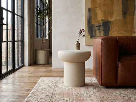 Pescocostanzo Cream Textured Fiberglass Mushroom Side Table beside a leather sofa in an industrial loft