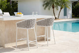 Two Petralia counter stools at a white quartz and travertine outdoor kitchen counter by a Naples pool, palms behind (counter not included)