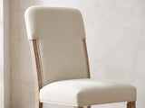 Close-up of the Picinisco 74-Inch Extendable Oak Veneer Dining Set with 4 Chairs: the tall upholstered back, exposed oak posts and padded seat of a chair in beige chenille