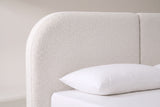 The rounded top corner of the Pietrabbondante headboard in ivory boucle, with the seam between the two panels and a white pillow below