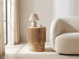 Pievepelago Natural Mango Fluted Drum Side Table with a lamp and a ceramic bowl beside a cream boucle armchair in a bright plaster room