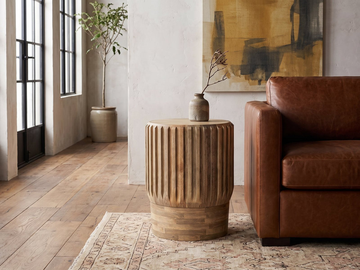 Pievepelago Natural Mango Fluted Drum Side Table beside a leather sofa in an industrial loft