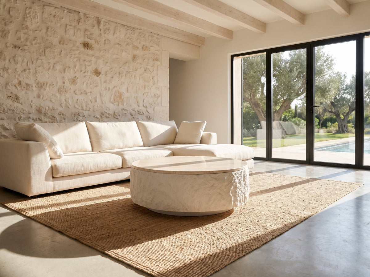 Piombino Faux Travertine Fiberglass Drum Coffee Table on a jute rug in front of a linen sofa in a poolside villa